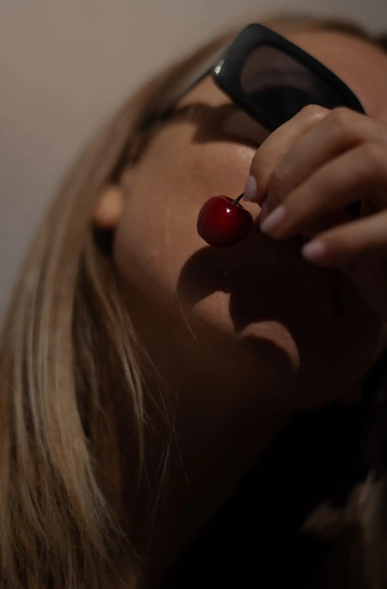 A glossy red cherry with a short stem, held delicately between fingers.