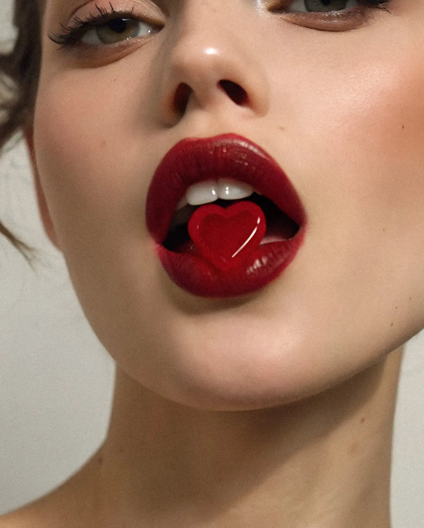 A glossy red heart-shaped candy held between full lips.