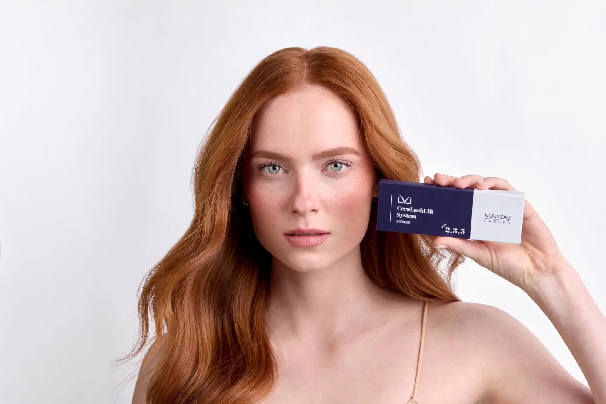 A young woman with long, wavy red hair holding a dark blue rectangular box with white text.